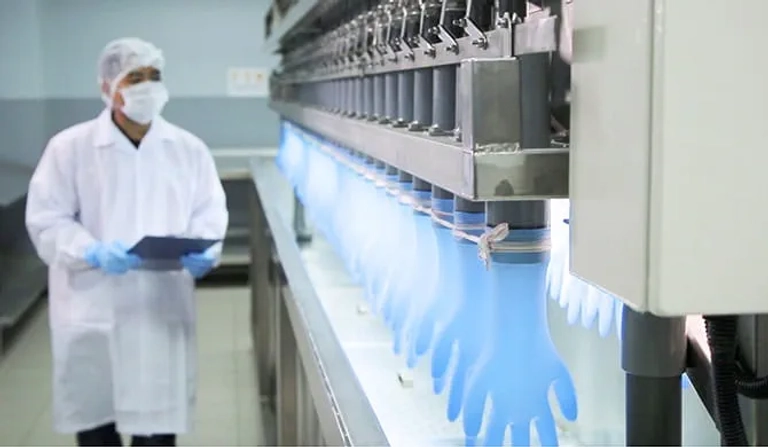 Technician inspects blue medical gloves being manufactured on an automated production line in a factory.