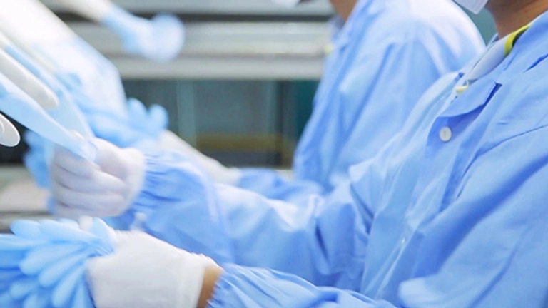 People in blue protective clothing and gloves work in a laboratory or cleanroom environment.
